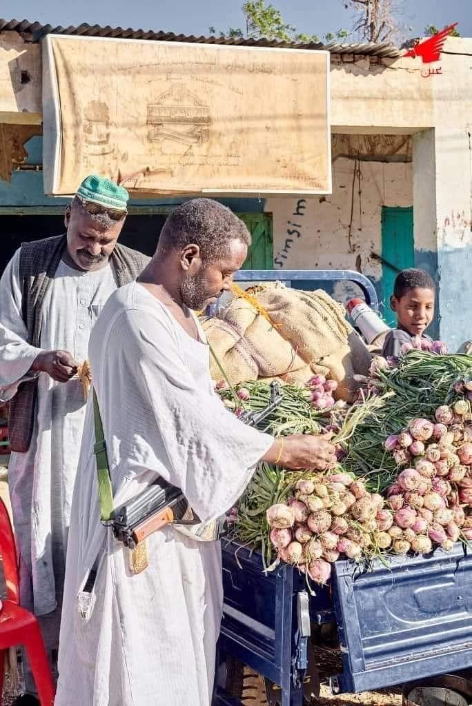 شاهد بالصور.. تجار الخضار وأصحاب المحلات وبائعو “الطعمية” بسوق شندي يحملون السلاح أثناء مباشرتهم لعملهم تحسباً لأي هجوم من “الدعامة”