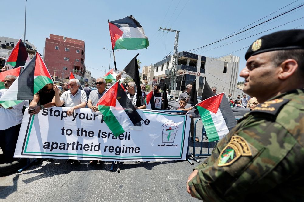 فلسطينيون يحملون لافته ضد الفصل العنصري الذي تمارسه اسرائيل بالضفة الغربية (رويترز)